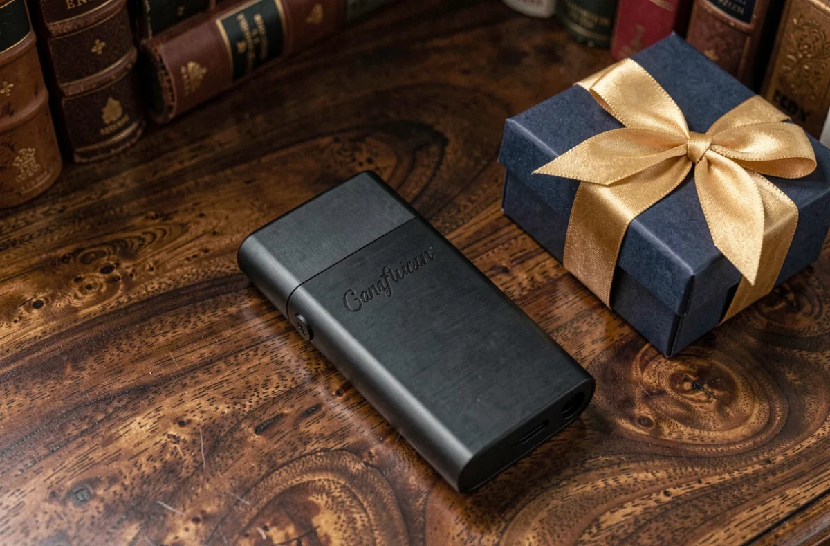 Briquet luxueux noir mat posé sur une surface en bois sombre avec une boîte cadeau élégante ruban doré